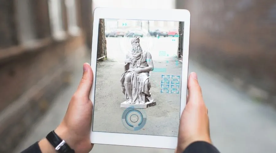 Manos sujetando una tablet que muestra una estatua en realidad aumentada en plena calle