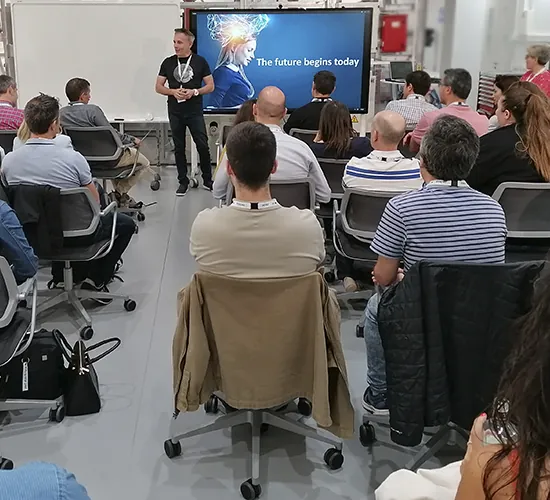Ponente presenta ante un grupo de empleados sentados frente a una pantalla en un hackathon corporativo