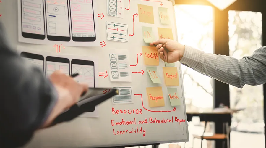 Pizarra con bocetos de pantallas de app y notas adhesivas durante un hackathon corporativo