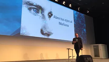 Ponente en el escenario con una pantalla que muestra el lema Abre tus ojos al mañana