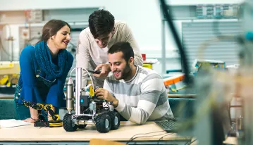 Tres compañeros montando y programando un pequeño robot con brazo articulado en un taller