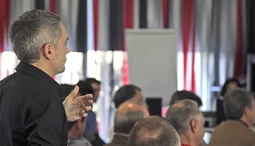 Formador gesticulando mientras se dirige a un grupo de asistentes durante un taller presencial