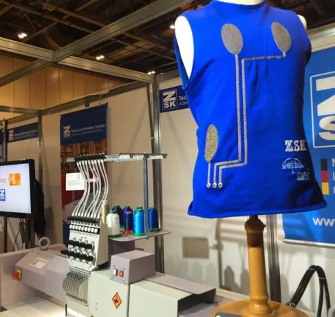 Camiseta inteligente con sensores bordados junto a una máquina de bordado técnico en una feria