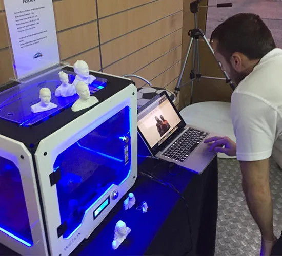 Hombre junto a una impresora 3D iluminada que imprime pequeños bustos blancos
