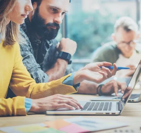 Equipo de consultoría revisando un proyecto en portátiles alrededor de una mesa de trabajo