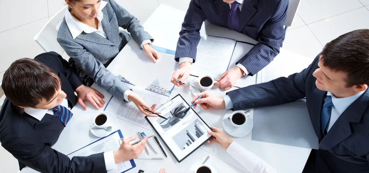 Reunión de trabajo vista desde arriba con gráficos de resultados y tazas de café