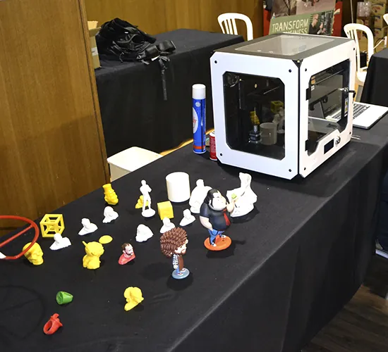 Impresora 3D junto a figuras impresas de colores sobre una mesa de exposición