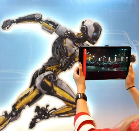 Persona sostiene una tablet con realidad aumentada frente a un gran mural de un robot