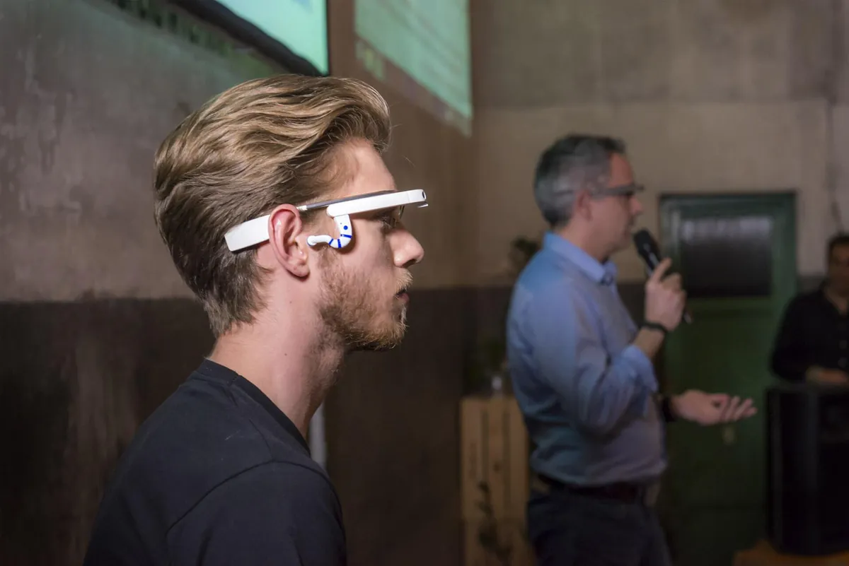 Joven probando unas gafas inteligentes mientras un ponente presenta con micrófono al fondo
